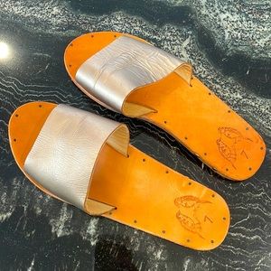 BEEK Gold leather slide sandal, wood sole on top and rubber on bottom.